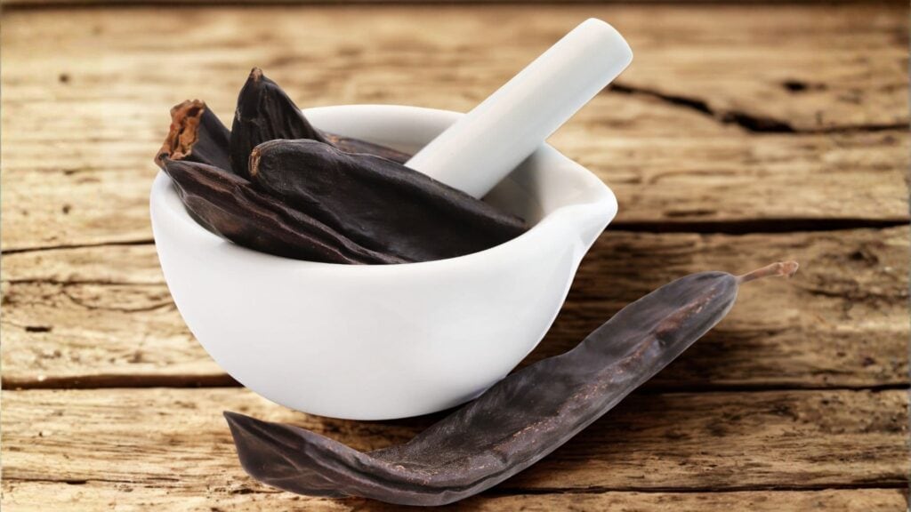 Gousses de caroube naturelles dans un bol sur une surface en bois