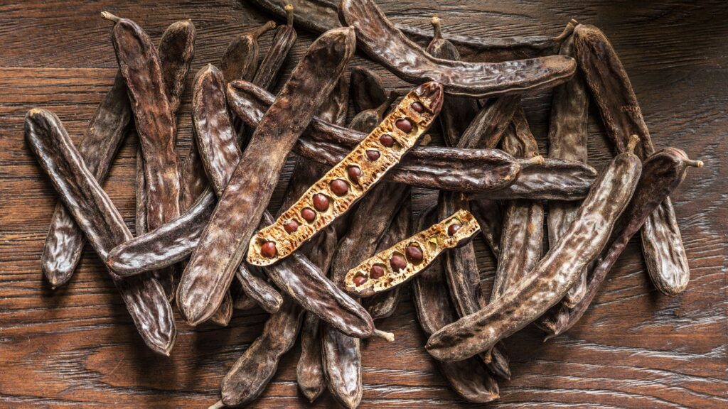 vagens de alfarroba sobre mesa de madeira rústica mostrando propriedades naturais da alfarroba