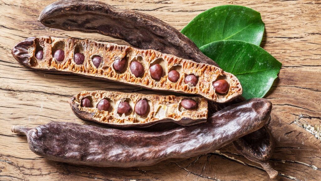 Carob pods on a rustic wooden table in natural sunlight